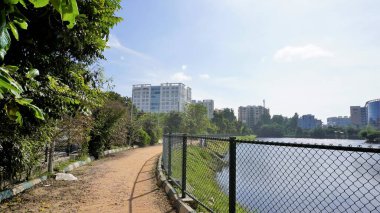 Bangalore, Karnataka, Hindistan-18 Eylül 2022: Yeşil kaplı ve bulutlu gökyüzü ve şehir altyapısı açık iblur gölünün yürüyüş şeridi.