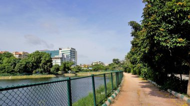 Bangalore, Karnataka, Hindistan-18 Eylül 2022: Yeşil kaplı ve bulutlu gökyüzü ve şehir altyapısı açık iblur gölünün yürüyüş şeridi.