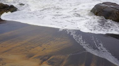 Muttom plajının güzel kayalık kıyısı. Sarı ve siyah kumlarda deniz dalgaları var..