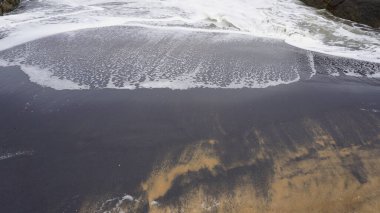 Muttom plajının güzel kayalık kıyısı. Sarı ve siyah kumlarda deniz dalgaları var..