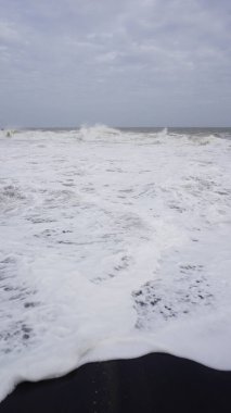 Muttom plajının güzel kayalık kıyısı. Sarı ve siyah kumlarda deniz dalgaları var..