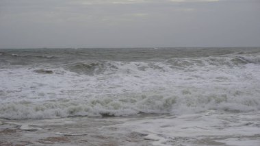 Muttom plajının güzel kayalık kıyısı. Sarı ve siyah kumlarda deniz dalgaları var..