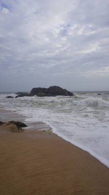 Muttom plajının güzel kayalık kıyısı. Sarı ve siyah kumlarda deniz dalgaları var..