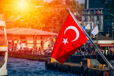 Gün batımında Türk bayrağı ve arka planda bulanık şehir manzarası.