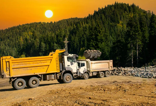 The excavator loads crushed stone in a dump truck body. Loading stones to a truck with an excavator in the forest.