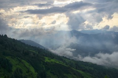 Gün batımı, bir fırtına koparken platoda son ışık demetlerini atıyor. Platonun üzerindeki siste bir köy.