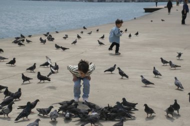 18.04.2024, İstanbul, Türkiye: Çocuk arka planda güvercinleri ve Boğaz manzarasını kovalıyor.