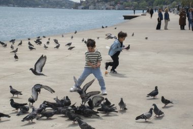 18.04.2024, İstanbul, Türkiye: Çocuk arka planda güvercinleri ve Boğaz manzarasını kovalıyor.