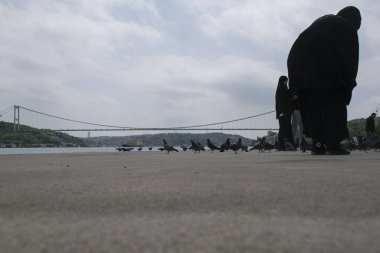 18.04.2024, İstanbul, Türkiye: Arka planda güvercinler, Boğazdaki insanlar ve Boğaz ve Fatih Sultan Mehmet Köprüsü manzarası