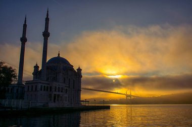 İstanbul 'daki Ortakoy Camii ve Boğaz Köprüsü. Dramatik bir gökyüzü. 15 Temmuz Şehitler Köprüsü sisli. Siste muhteşem İstanbul manzarası.