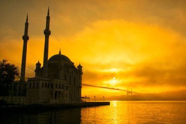 Sisli bir sabahta boğazın üzerinde uçan güvercinler. 15 Temmuz Şehitler Köprüsü ve Ortakoy Camii siste. 