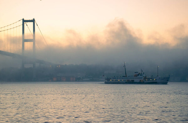 Вид на мост Мучеников 15 июля с чайкой и восходом солнца в туманных облаках. Паром по городским линиям, плывущий в Туманном проливе и под Босфорским мостом.