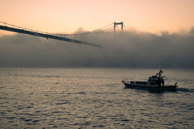 15 Temmuz Şehitler Köprüsü (Boğaz Köprüsü), sis bulutlarında martı ve gün doğumuyla birlikte görülüyor. Sisli boğazda balıkçı tekneleri.