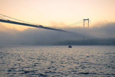 15 Temmuz Şehitler Köprüsü (Boğaz Köprüsü), sis bulutlarında martı ve gün doğumuyla birlikte görülüyor. Sisli boğazda balıkçı tekneleri.