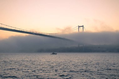 15 Temmuz Şehitler Köprüsü (Boğaz Köprüsü), sis bulutlarında martı ve gün doğumuyla birlikte görülüyor. Sisli boğazda balıkçı tekneleri.