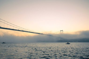 15 Temmuz Şehitler Köprüsü (Boğaz Köprüsü), sis bulutlarında martı ve gün doğumuyla birlikte görülüyor. Sisli boğazda balıkçı tekneleri.