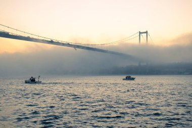 15 Temmuz Şehitler Köprüsü (Boğaz Köprüsü), sis bulutlarında martı ve gün doğumuyla birlikte görülüyor. Sisli boğazda balıkçı tekneleri.