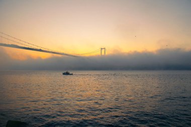 15 Temmuz Şehitler Köprüsü (Boğaz Köprüsü), sis bulutlarında martı ve gün doğumuyla birlikte görülüyor. Sisli boğazda balıkçı tekneleri.