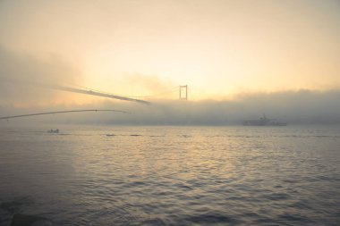 15 Temmuz Şehitler Köprüsü (Boğaz Köprüsü), sis bulutlarında martı ve gün doğumuyla birlikte görülüyor. Sisli boğazda balıkçı tekneleri.