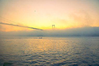15 Temmuz Şehitler Köprüsü (Boğaz Köprüsü), sis bulutlarında martı ve gün doğumuyla birlikte görülüyor. Sisli boğazda balıkçı tekneleri.