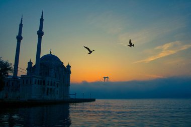 15 Temmuz Şehitler Köprüsü (Boğaz Köprüsü), sis bulutlarında martı ve gün doğumuyla birlikte görülüyor. Ortakoy Camii ve Boğaz Köprüsü 'nden sisli sabah manzarası