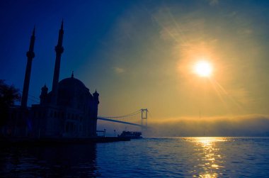 İstanbul 'daki Ortakoy Camii ve Boğaz Köprüsü. Dramatik bir gökyüzü. 15 Temmuz Şehitler Köprüsü sisli. Sisli bir günde Denizdeki Yolcu Gemisi.