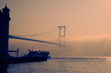 İstanbul 'daki Ortakoy Camii ve Boğaz Köprüsü. Dramatik bir gökyüzü. 15 Temmuz Şehitler Köprüsü sisli. Sisli bir günde Denizdeki Yolcu Gemisi.