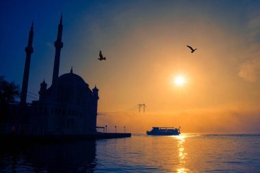 İstanbul 'daki Ortakoy Camii ve Boğaz Köprüsü. Dramatik bir gökyüzü. 15 Temmuz Şehitler Köprüsü sisli. Sisli bir günde Denizdeki Yolcu Gemisi.