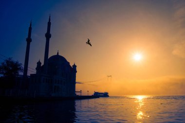 İstanbul 'daki Ortakoy Camii ve Boğaz Köprüsü. Dramatik bir gökyüzü. 15 Temmuz Şehitler Köprüsü sisli. Sisli bir günde Denizdeki Yolcu Gemisi.