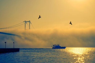 15 Temmuz Şehitler Köprüsü ve Ortaklık Camii 'nin gün doğumu manzarası. 15 Temmuz Şehitler Köprüsü 'nün altında sisli boğazda bir yat hareket ediyor..