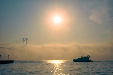 15 Temmuz Şehitler Köprüsü ve Ortaklık Camii 'nin gün doğumu manzarası. 15 Temmuz Şehitler Köprüsü 'nün altında sisli boğazda bir yat hareket ediyor..