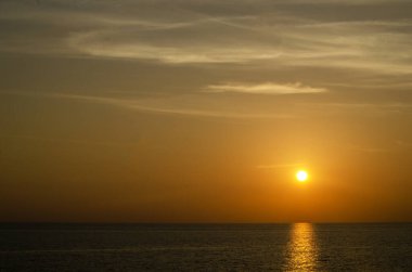 Phuket, Tayland 'da okyanusun üzerinde güzel bir gün batımı, durgun suya yansıyan renkli gökyüzü. Canlı turuncu ve pembe renkleri olan tropik bir cennet. Seyahat ve tatil temaları için mükemmel..