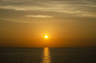 Phuket, Tayland 'da okyanusun üzerinde güzel bir gün batımı, durgun suya yansıyan renkli gökyüzü. Canlı turuncu ve pembe renkleri olan tropik bir cennet. Seyahat ve tatil temaları için mükemmel..