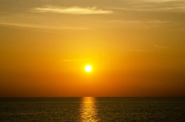 Phuket, Tayland 'da okyanusun üzerinde güzel bir gün batımı, durgun suya yansıyan renkli gökyüzü. Canlı turuncu ve pembe renkleri olan tropik bir cennet. Seyahat ve tatil temaları için mükemmel..