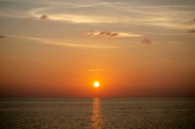 Phuket, Tayland 'da okyanusun üzerinde güzel bir gün batımı, durgun suya yansıyan renkli gökyüzü. Canlı turuncu ve pembe renkleri olan tropik bir cennet. Seyahat ve tatil temaları için mükemmel..