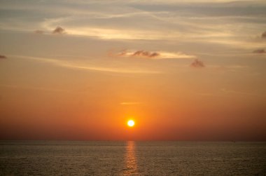 Phuket, Tayland 'da okyanusun üzerinde güzel bir gün batımı, durgun suya yansıyan renkli gökyüzü. Canlı turuncu ve pembe renkleri olan tropik bir cennet. Seyahat ve tatil temaları için mükemmel..
