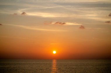 Phuket, Tayland 'da okyanusun üzerinde güzel bir gün batımı, durgun suya yansıyan renkli gökyüzü. Canlı turuncu ve pembe renkleri olan tropik bir cennet. Seyahat ve tatil temaları için mükemmel..
