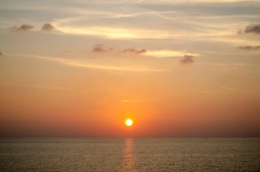 Phuket, Tayland 'da okyanusun üzerinde güzel bir gün batımı, durgun suya yansıyan renkli gökyüzü. Canlı turuncu ve pembe renkleri olan tropik bir cennet. Seyahat ve tatil temaları için mükemmel..