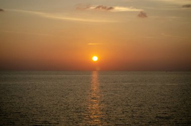 Phuket, Tayland 'da okyanusun üzerinde güzel bir gün batımı, durgun suya yansıyan renkli gökyüzü. Canlı turuncu ve pembe renkleri olan tropik bir cennet. Seyahat ve tatil temaları için mükemmel..