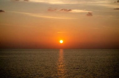 Phuket, Tayland 'da okyanusun üzerinde güzel bir gün batımı, durgun suya yansıyan renkli gökyüzü. Canlı turuncu ve pembe renkleri olan tropik bir cennet. Seyahat ve tatil temaları için mükemmel..