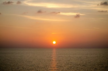 Phuket, Tayland 'da okyanusun üzerinde güzel bir gün batımı, durgun suya yansıyan renkli gökyüzü. Canlı turuncu ve pembe renkleri olan tropik bir cennet. Seyahat ve tatil temaları için mükemmel..