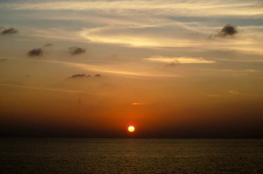 Phuket, Tayland 'da okyanusun üzerinde güzel bir gün batımı, durgun suya yansıyan renkli gökyüzü. Canlı turuncu ve pembe renkleri olan tropik bir cennet. Seyahat ve tatil temaları için mükemmel..