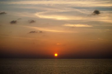 Phuket, Tayland 'da okyanusun üzerinde güzel bir gün batımı, durgun suya yansıyan renkli gökyüzü. Canlı turuncu ve pembe renkleri olan tropik bir cennet. Seyahat ve tatil temaları için mükemmel..