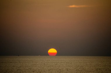 Phuket, Tayland 'da okyanusun üzerinde güzel bir gün batımı, durgun suya yansıyan renkli gökyüzü. Canlı turuncu ve pembe renkleri olan tropik bir cennet. Seyahat ve tatil temaları için mükemmel..