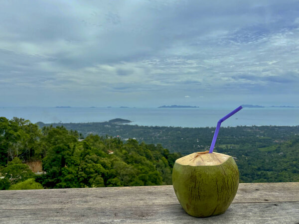 Кокос с соломинкой на деревянном столе с видом на остров Самуи с террасы дома на холме Липа Ной, Ко Самуи