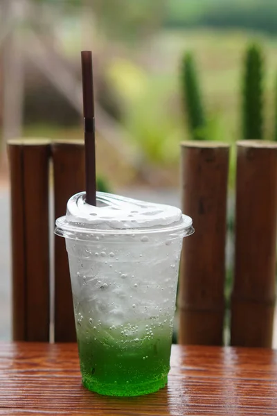 stock image green soda in plastic cup on wooden table, blur nature background, food, drink, fresh, cool, copy space                        