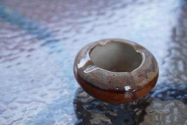 Cam masa zemininde küçük kahverengi yuvarlak seramik kül tablası, nesne, dekor, klasik, rahat, sigara, kopyalama alanı                           