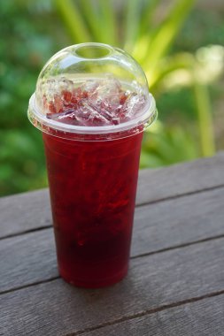 front view roselle juice in a plastic glass, on a wooden floor, blur green nature background, food, drink, object, copy space                                         