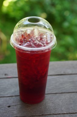 Roselle juice in a plastic glass, on a wooden floor, blur green nature background, food, drink, object, copy space                             