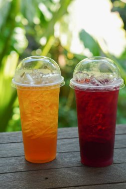 Roselle juice and Chrysanthemum juice in a plastic glass, on a wooden floor, blur green nature background, food, drink, object, copy space                                            